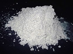 Close-up image of diatomaceous earth powder in a glass jar with a wooden spoon, showing its fine, chalky texture used for natural pest control and household uses.